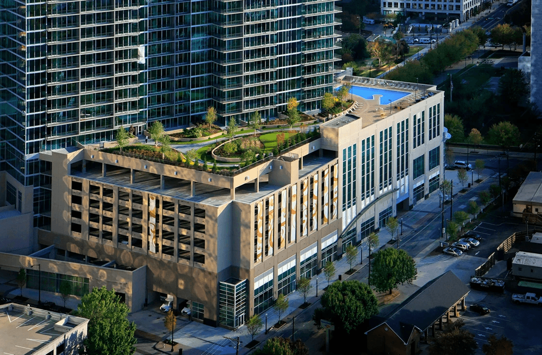 Aerial view of a modern building complex with rooftop gardens, a rooftop pool, and multi-level parking garage