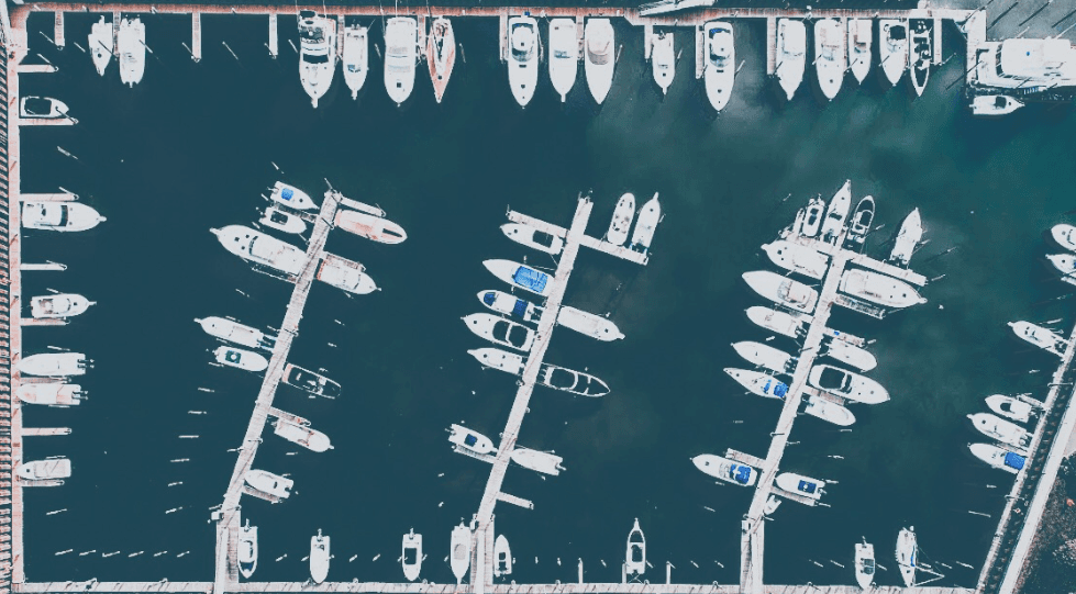 Aerial view of a marina with boats docked on both sides of multiple piers in blue water