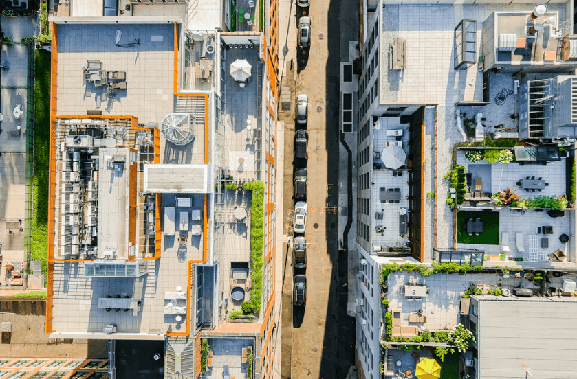 Aerial view of city rooftops with a narrow street and parked cars between tall buildings