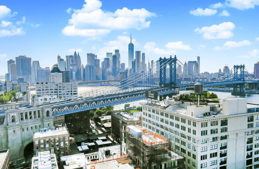 Drone shot of a city skyline with a large suspension bridge over a river and tall buildings