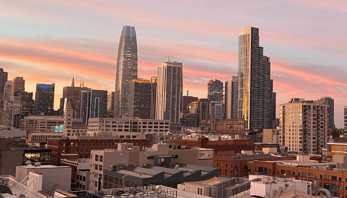 City skyline at sunset with tall glass skyscrapers, seen from a rooftop with lower buildings in foreground