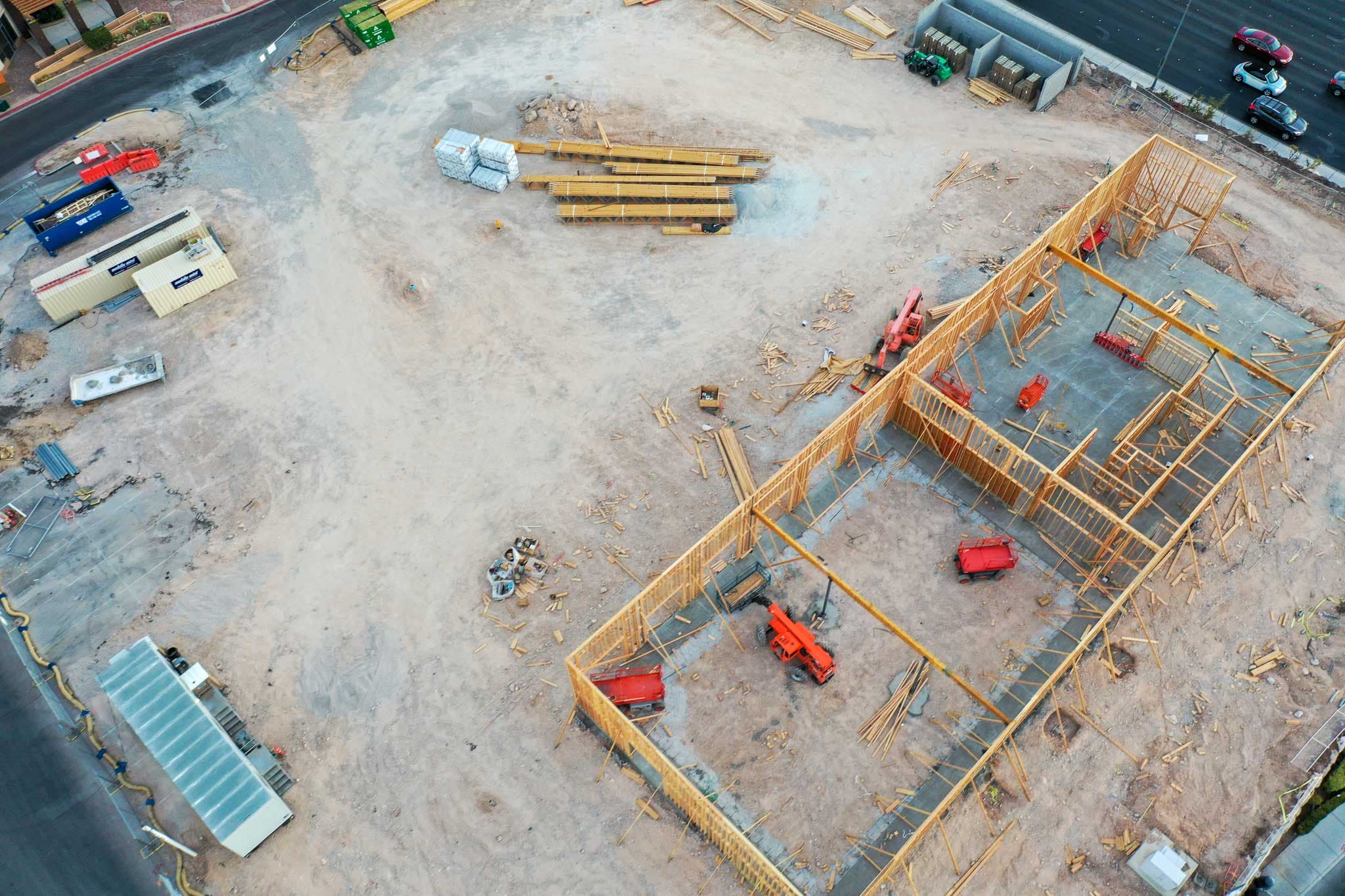 Aerial view of a construction site with wooden framing, lumber piles, and construction equipment