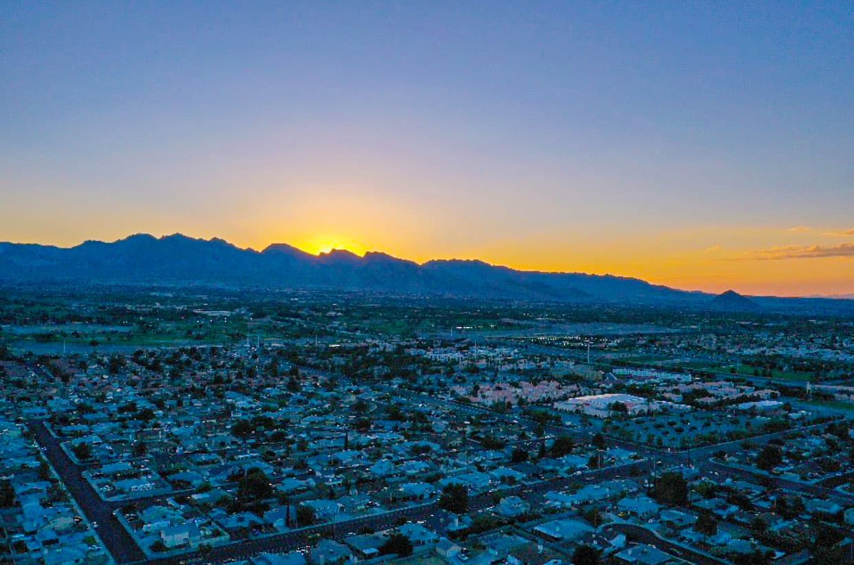 An aerial view of a grid-like suburban town at sunset with a distant mountain range on the horizon