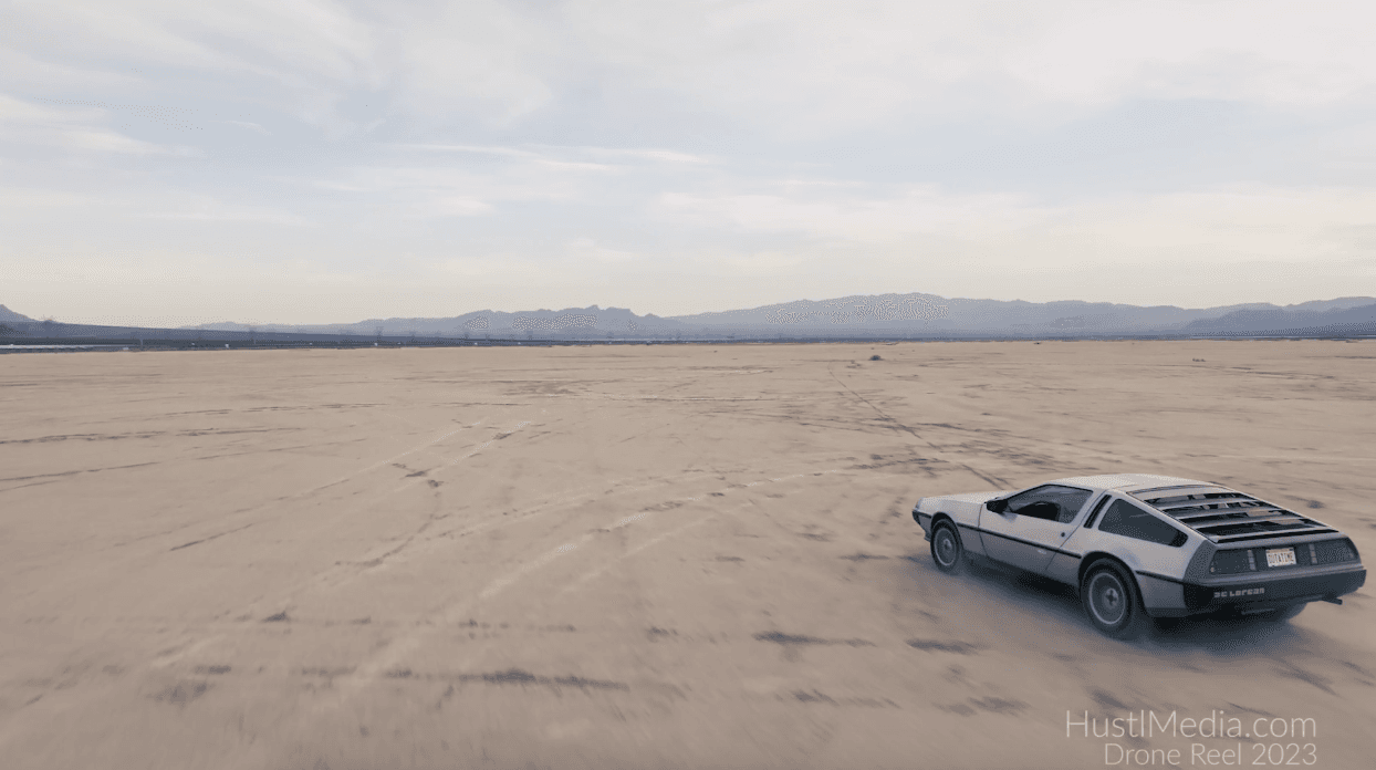 DeLorean sports car kicking up dust in a desert, with distant mountains; HustlMedia watermark