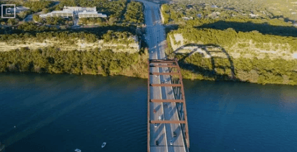 Aerial view of a steel truss bridge over a blue river with green banks and a road across