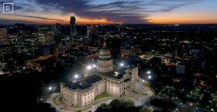 Aerial view of a domed neoclassical government building lit at dusk, with surrounding city lights