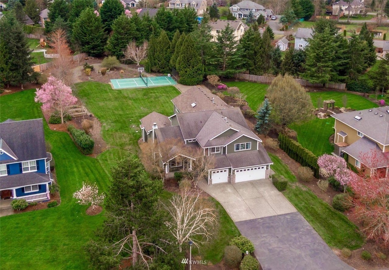 Aerial view of a suburban home with a three-car garage, green lawns, and a backyard basketball court