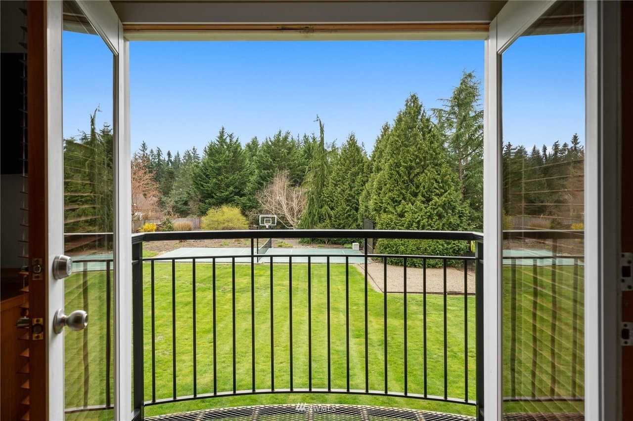 View from a doorway onto a curved balcony railing, green lawn, and distant basketball court with evergreens