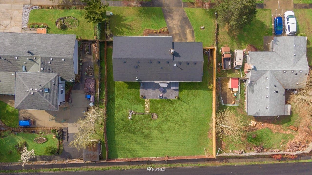 Aerial view of three houses with green lawns, fenced backyards, and parked cars