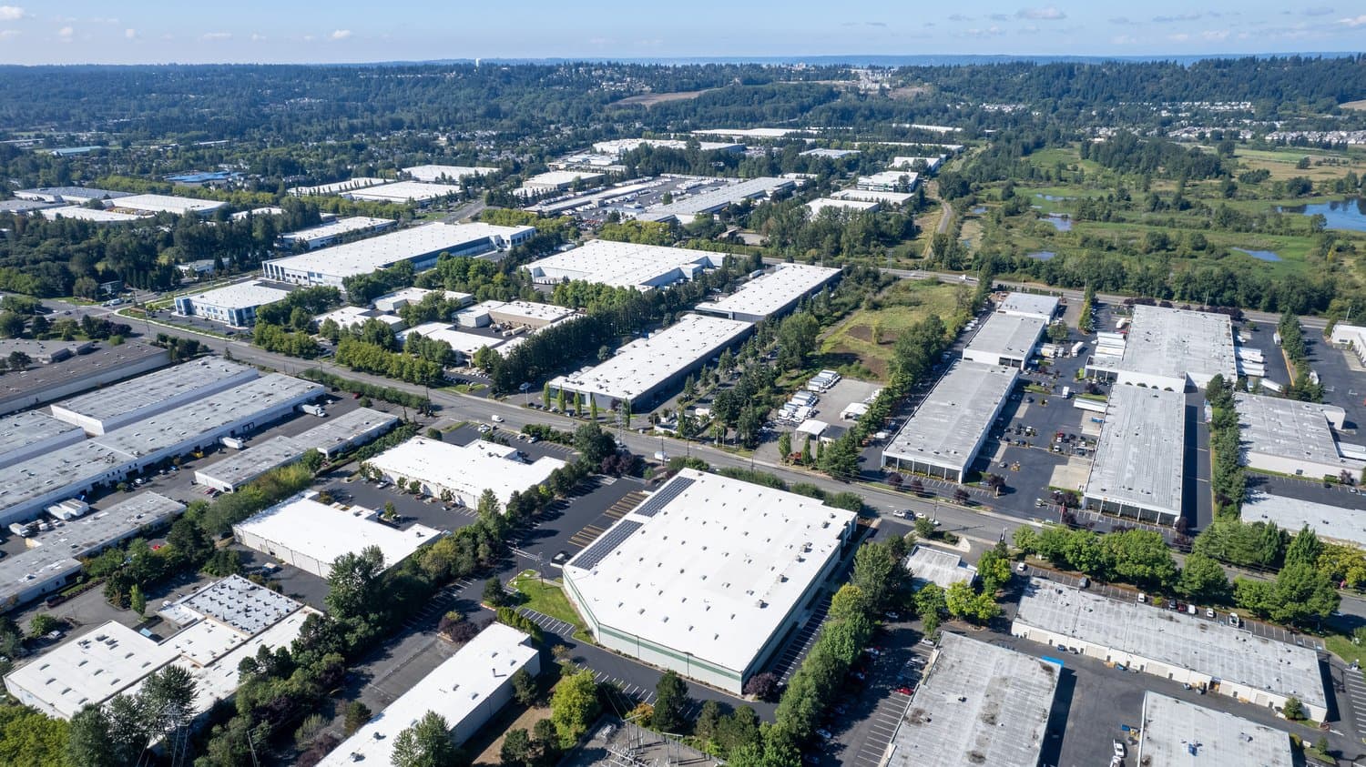 Aerial view of a large industrial park with white-roofed warehouses and tree-lined roads