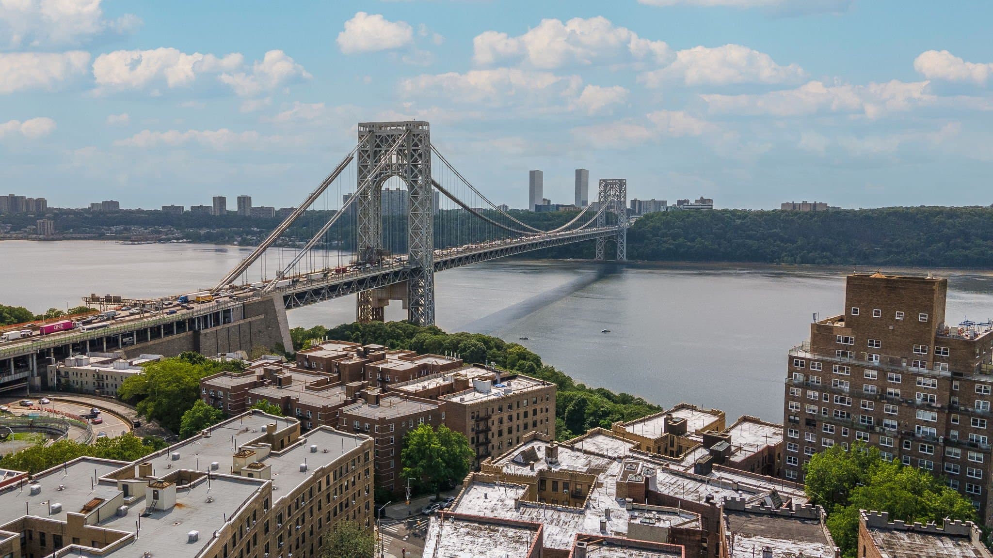 Suspension bridge with twin towers crossing a wide river, city skyline beyond