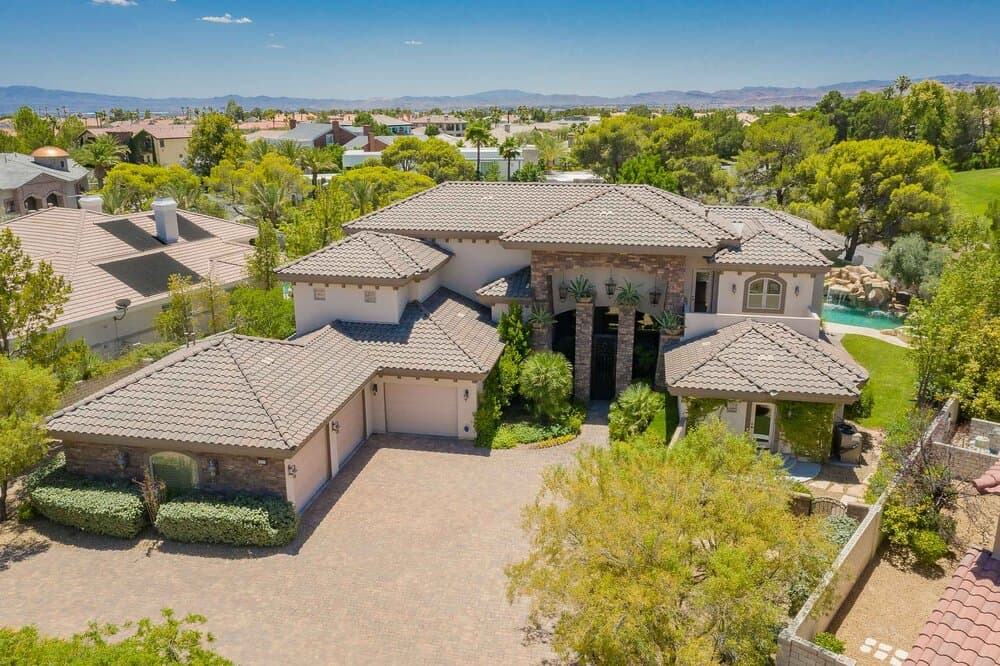 Aerial view of a large two-story house with tiled roof, stone facade, and a brick driveway