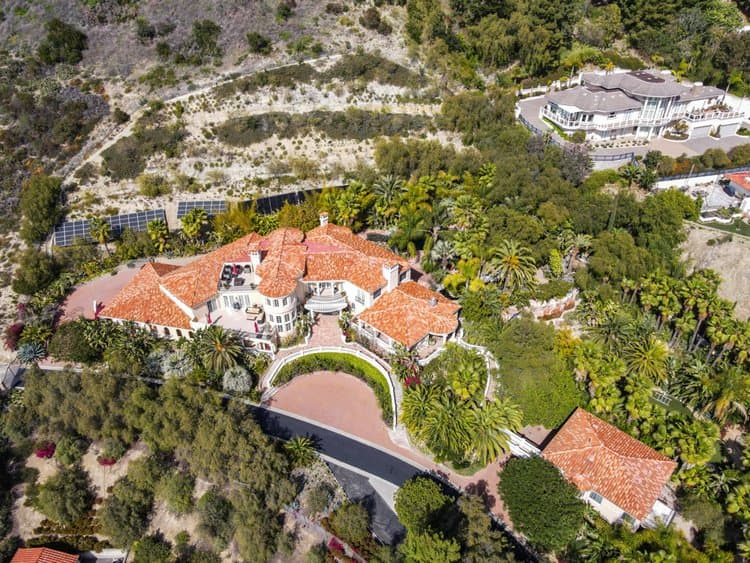 Drone aerial view of a villa with red tile roofs, curved driveway, and palm trees