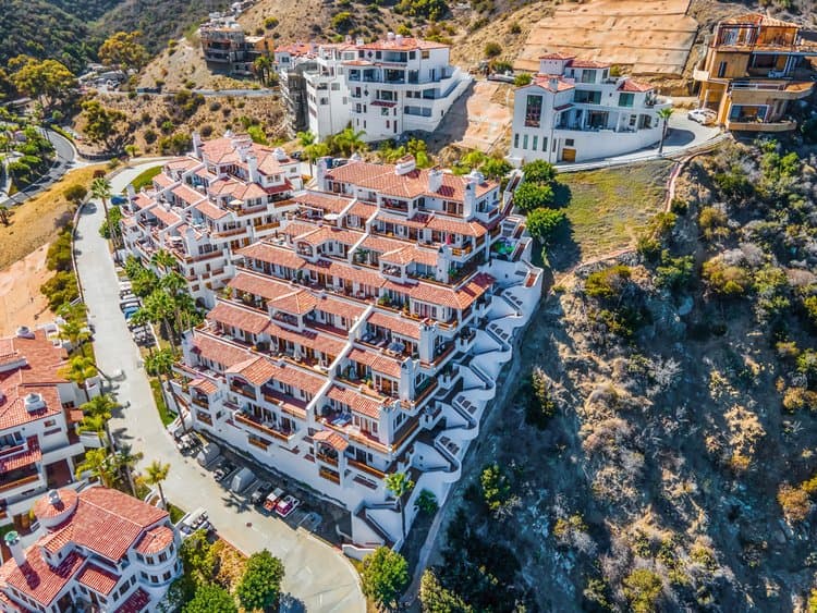 Drone aerial view of a white multi level villa complex with red tile roofs on a hillside
