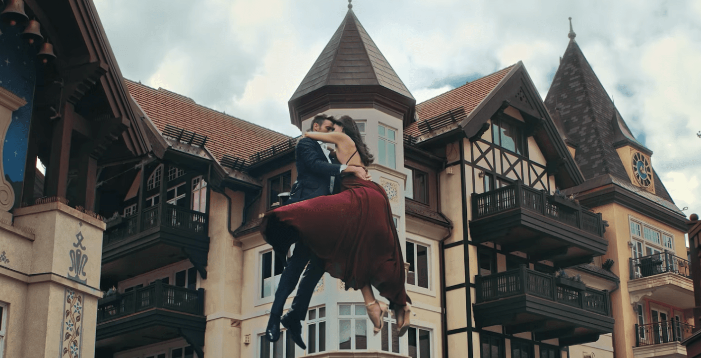 Couple in formal attire embracing midair in front of a castle-like building with balconies