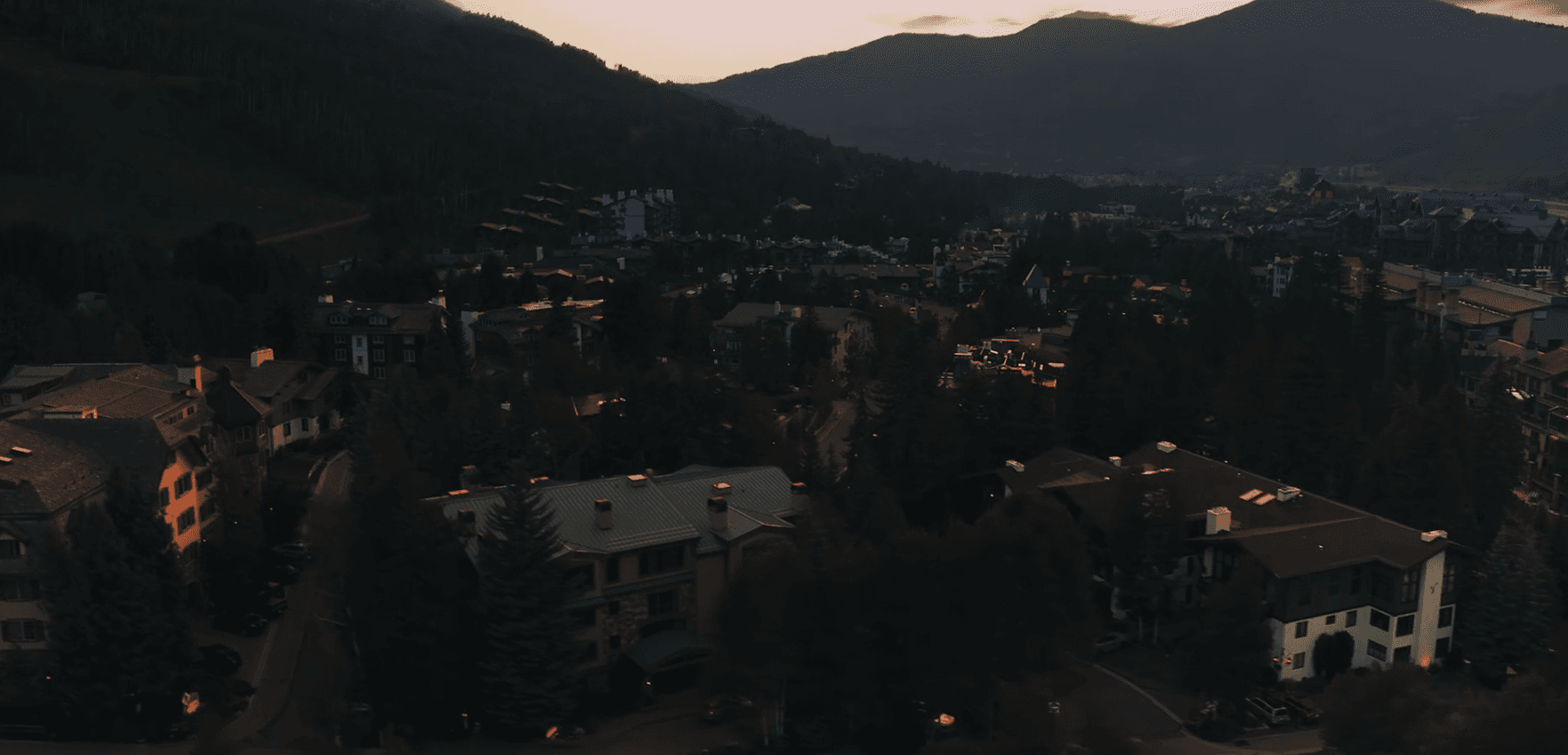 Aerial view of a hillside town at dusk with houses, trees and distant mountains