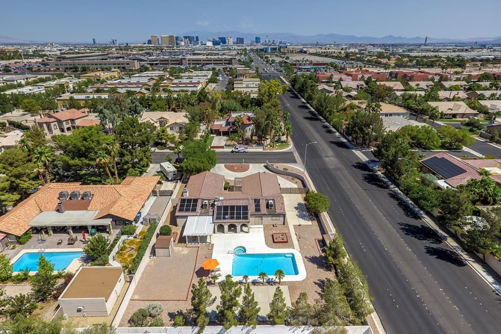 Aerial view of a suburban neighborhood with a central road, houses, and swimming pools