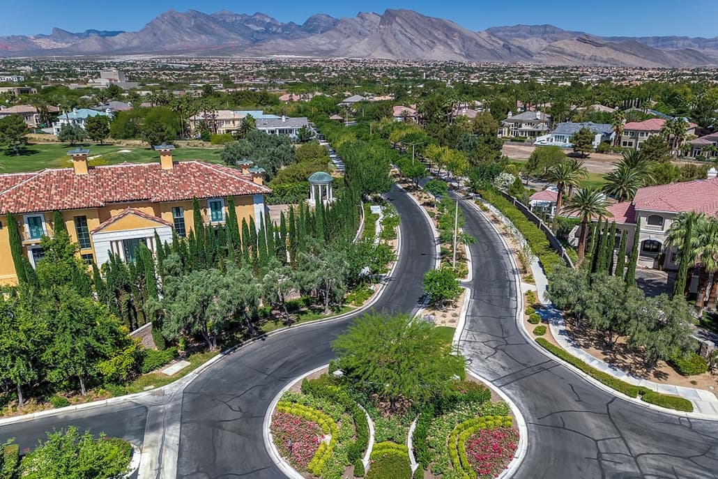 Curved suburban street with a landscaped roundabout, palm trees and Mediterranean houses, distant mountains