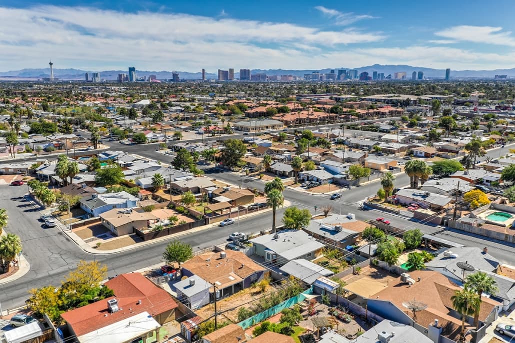 Aerial view of a suburban neighborhood with many houses, streets, and a distant city skyline on the horizon