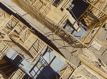 Aerial view of an unfinished wooden building frame with scaffolding and shadows