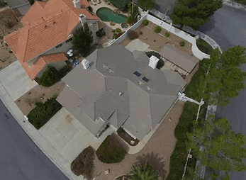 Aerial view of a house with a multi-gabled gray roof, beige exterior, and a curved backyard pool