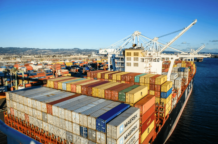 Aerial view of a cargo ship loaded with colorful shipping containers, port cranes overhead