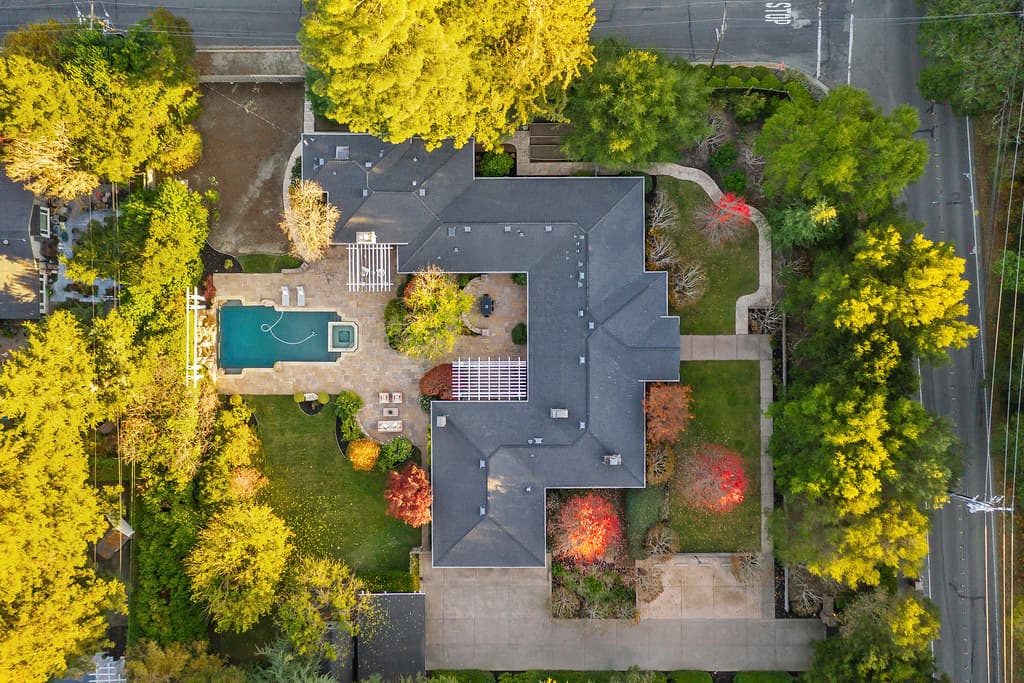 Aerial view of a large house with a backyard pool, surrounding trees, and a curved driveway