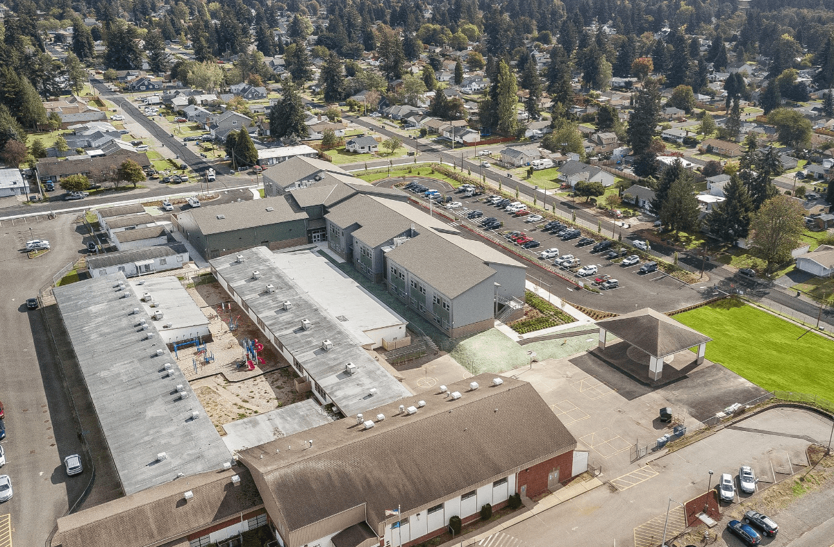 Aerial view of a school campus with connected buildings, a parking lot, playground, and surrounding houses