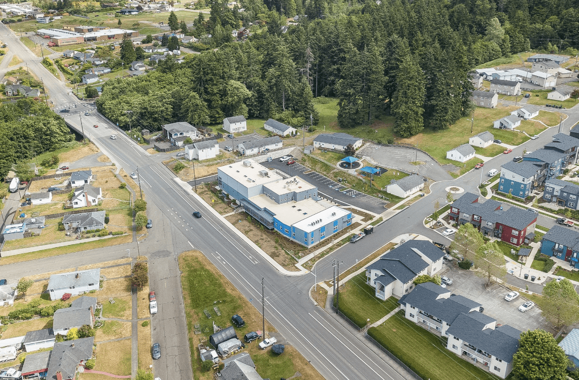 Aerial view of a small town with a blue and white building by a broad road, surrounded by houses and trees