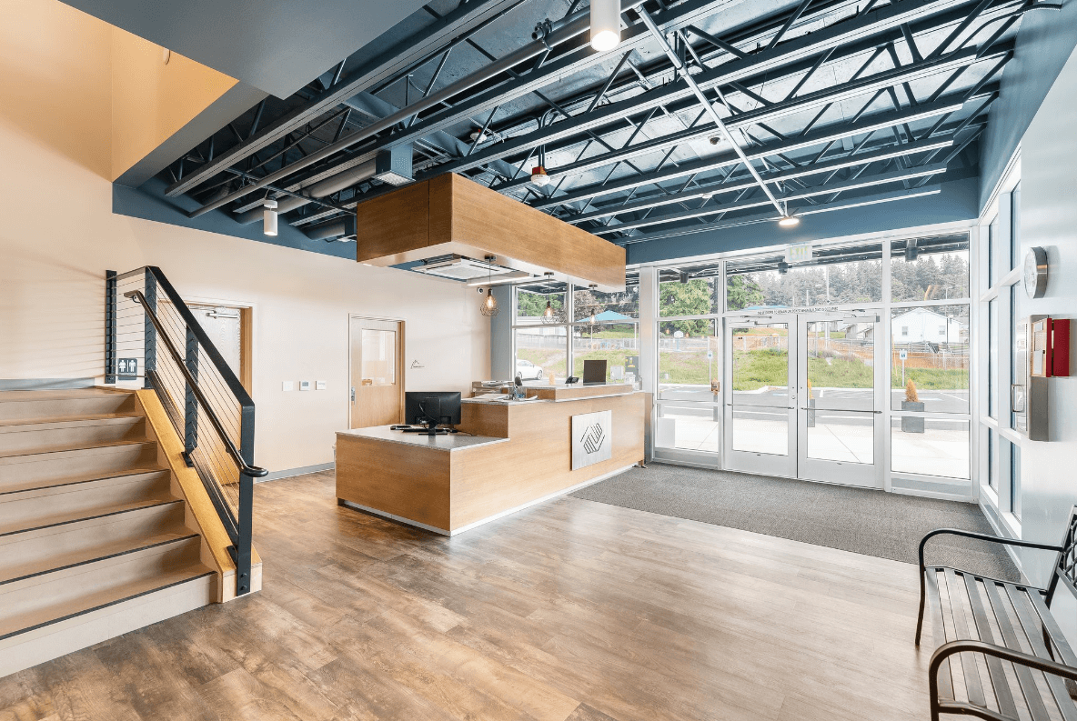 Lobby reception area with wooden desk, staircase, blue exposed ceiling and metal beams, and glass doors