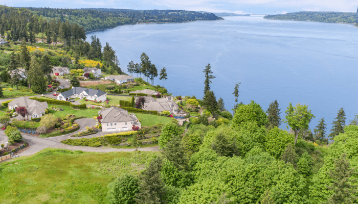 Aerial view of a lakeside neighborhood with houses, manicured lawns and trees beside a large blue lake