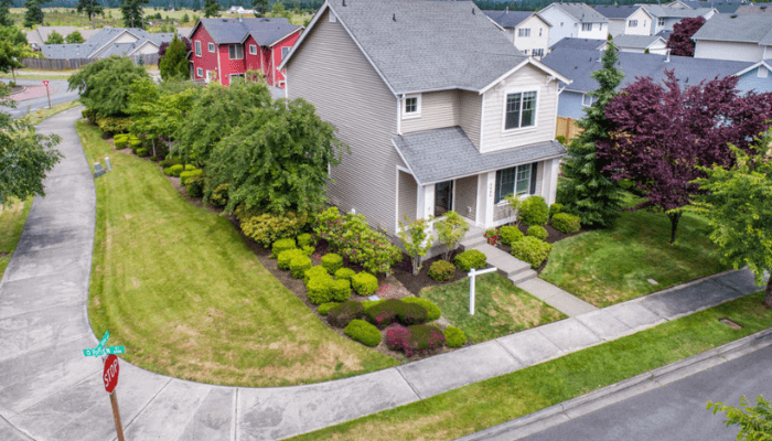 Aerial view of a beige two-story house with a gray roof, manicured front yard, and curved sidewalk