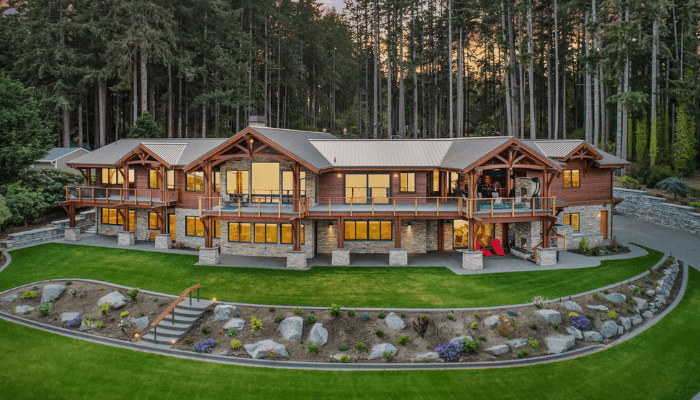 Two-story wooden lodge with stone foundation and balconies, curved lawn, rock garden, forest backdrop