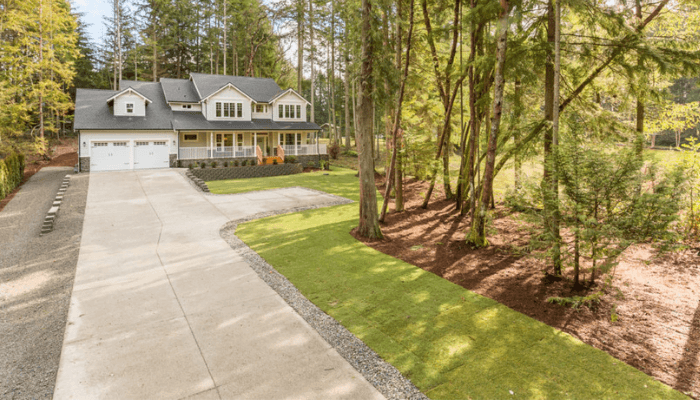 Two-story house with a two-car garage, front porch, curved driveway, and surrounding trees