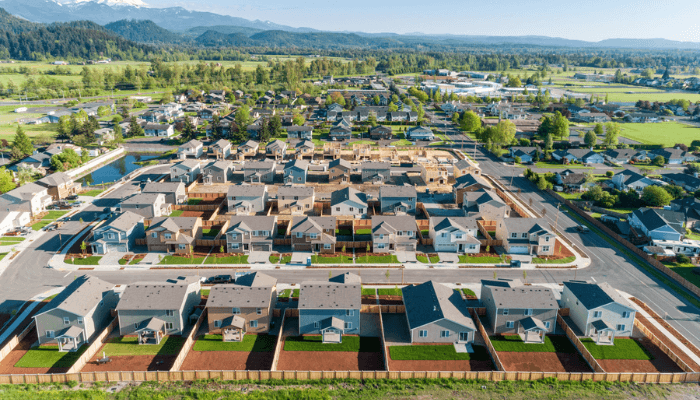 Aerial view of a suburban housing development with rows of houses and fenced backyards with distant mountains