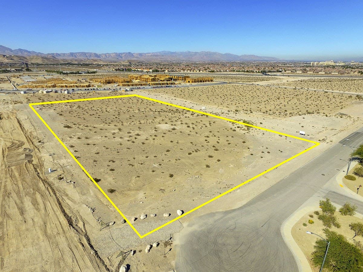 A desert lot outlined in yellow, viewed from above, with surrounding road, distant construction and mountains