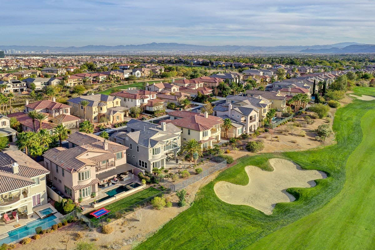 Drone shot of a suburban neighborhood along a golf course, with backyards, pools, bunkers, and mountains