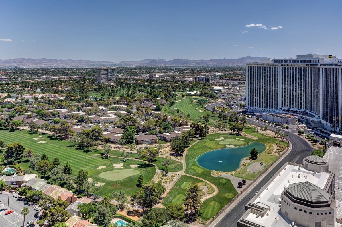 Aerial view of a large hotel beside a golf course, with green fairways, ponds, and surrounding houses